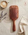 Wooden hairbrush on a textured surface with a cup of coffee and lavender flowers.
