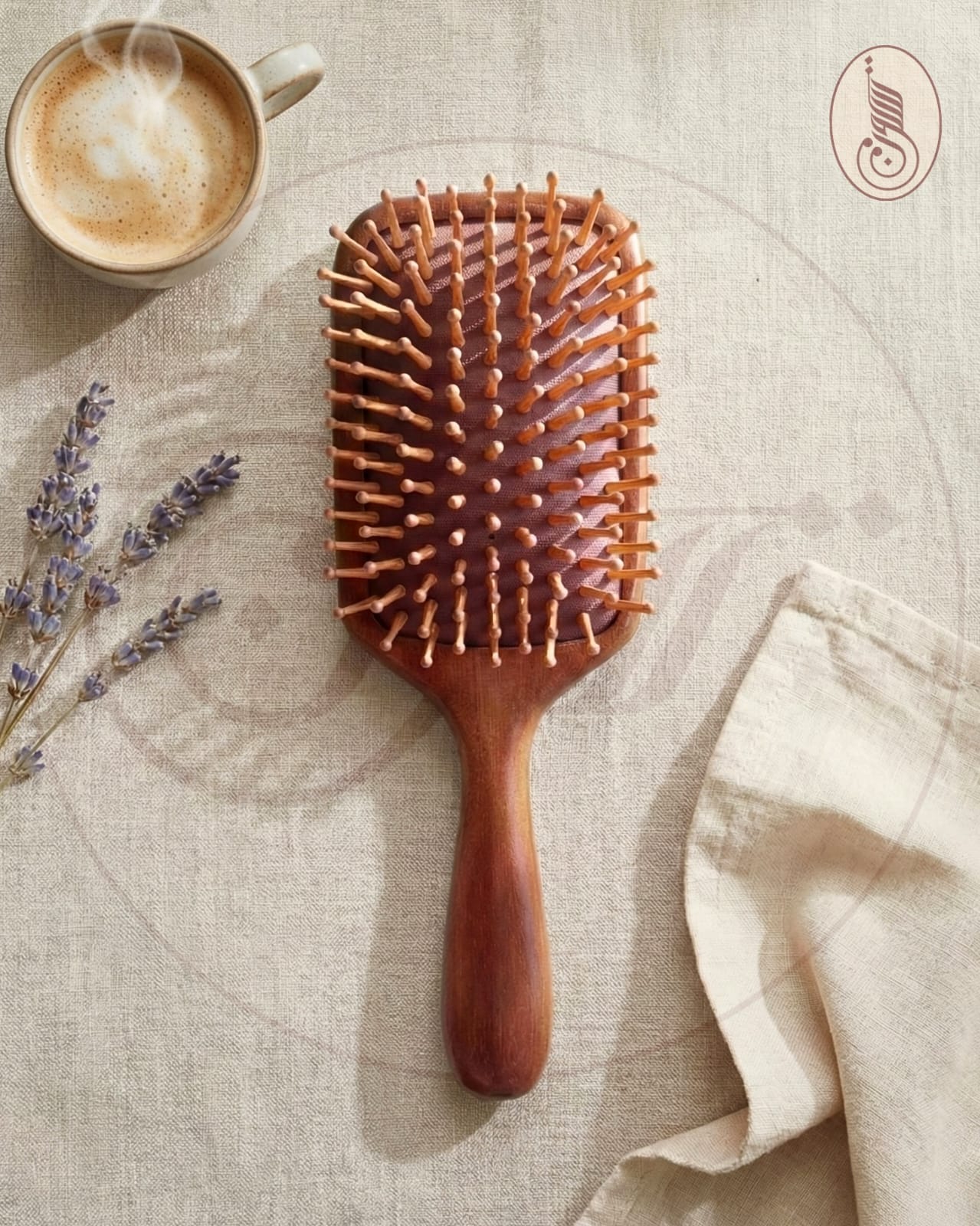 Wooden hairbrush on a textured surface with a cup of coffee and lavender flowers.