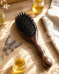 Wooden hairbrush with small jars of oil and lavender flowers on a wooden surface